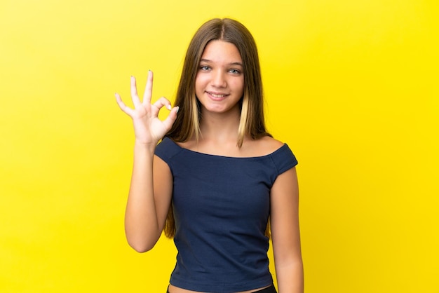 Little caucasian girl isolated on yellow background showing ok sign with fingers