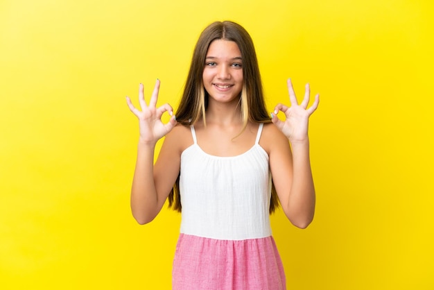 두 손으로 확인 표시를 보여주는 노란색 배경에 고립 된 어린 백인 소녀