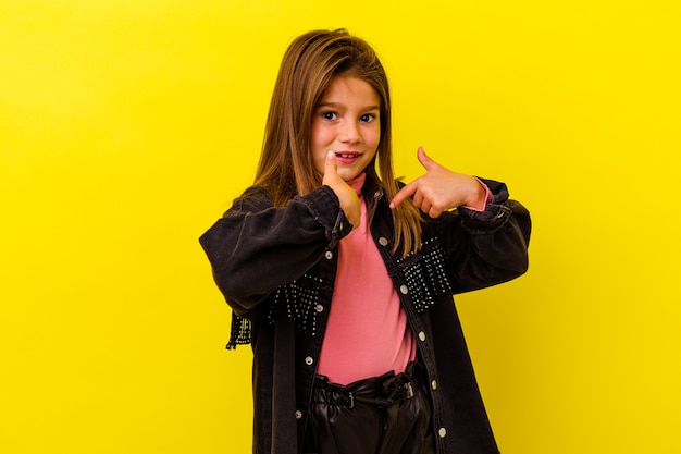 Little caucasian girl isolated on yellow background surprised pointing with finger, smiling broadly.