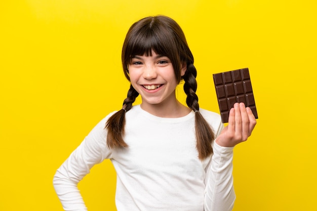 Little caucasian girl isolated on yellow background taking a
chocolate tablet and happy