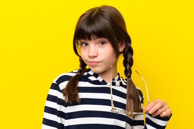 Little caucasian girl isolated on yellow background With glasses with happy expression