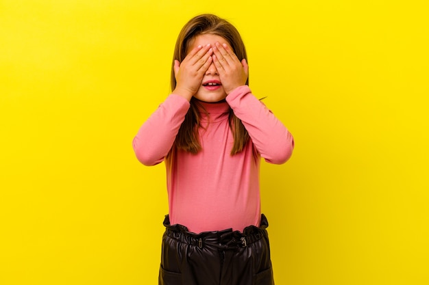 Photo little caucasian girl isolated on yellow covers eyes with hands, smiles broadly waiting for a surprise.