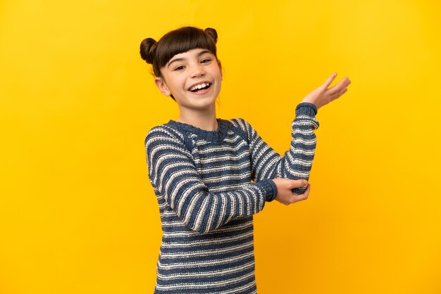 Little caucasian girl isolated on yellow extending hands to the side for inviting to come