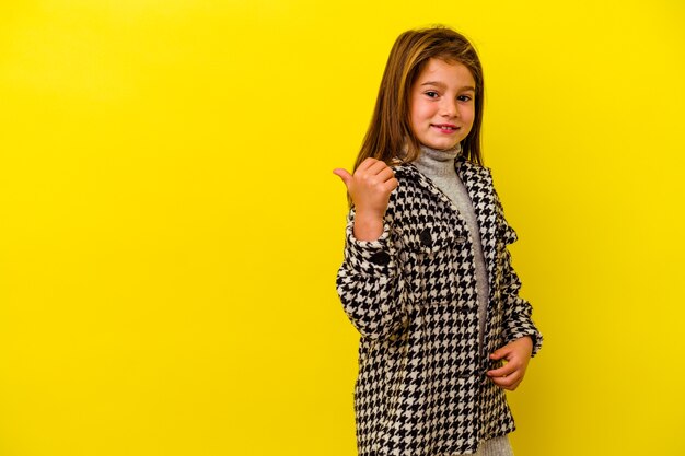 Little caucasian girl isolated on yellow points with thumb finger away, laughing and carefree