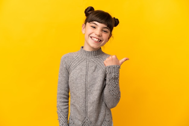 Little caucasian girl isolated on yellow wall pointing to the side to present a product