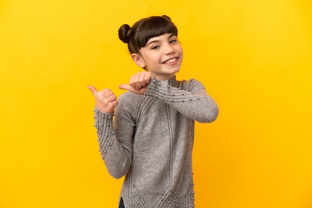 Little caucasian girl isolated on yellow wall pointing to the side to present a product