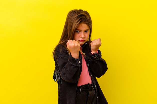 Piccola ragazza caucasica isolata sulla parete gialla che mostra il pugno alla macchina fotografica, espressione facciale aggressiva.