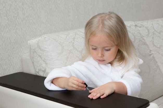 Little Caucasian girl paints nails on hands.