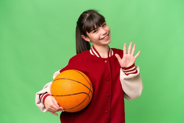 Little caucasian girl playing basketball over isolated background counting five with fingers