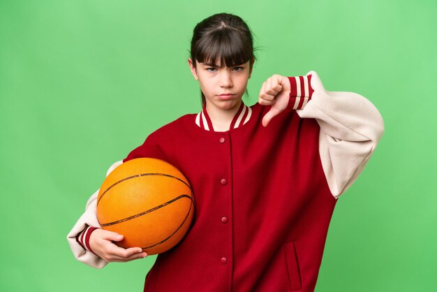 Little caucasian girl playing basketball over isolated background showing thumb down with negative expression