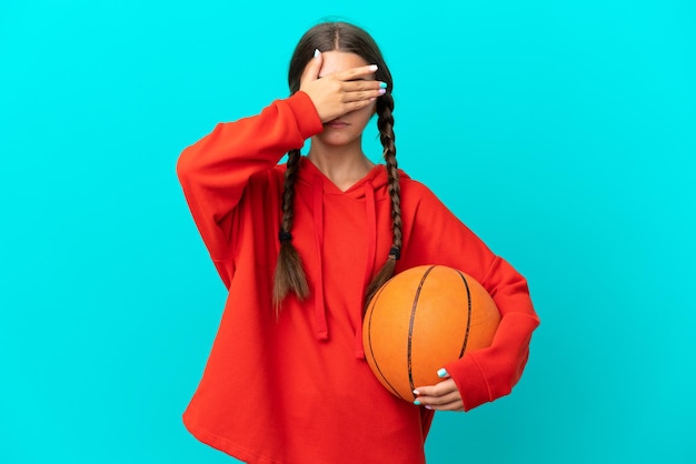 Little caucasian girl playing basketball isolated on blue background covering eyes by hands Do not want to see something