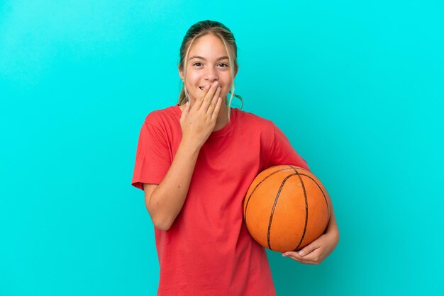 Little caucasian girl playing basketball isolated on blue background happy and smiling covering mouth with hand