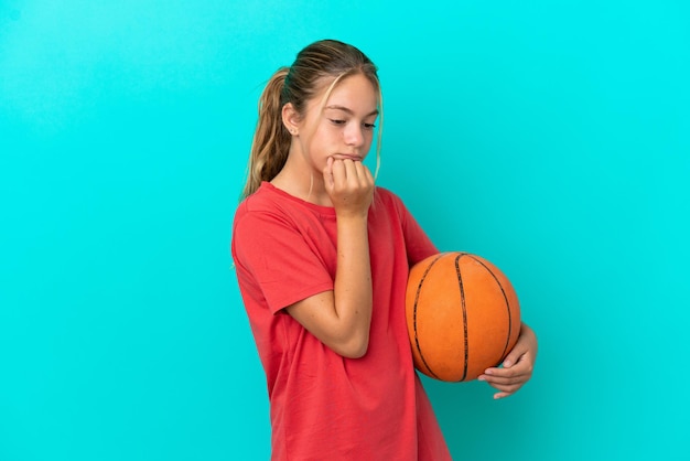 Little caucasian girl playing basketball isolated on blue background having doubts