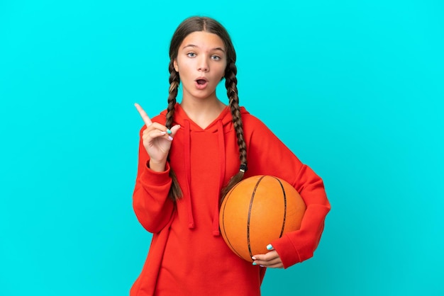 파란색 배경에 격리된 농구를 하는 백인 소녀는 손가락을 들어올리면서 해결책을 실현하려고 합니다