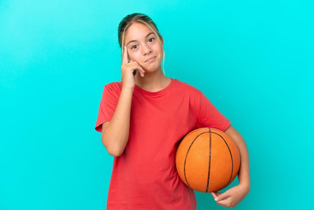 Little caucasian girl playing basketball isolated on blue background thinking an idea