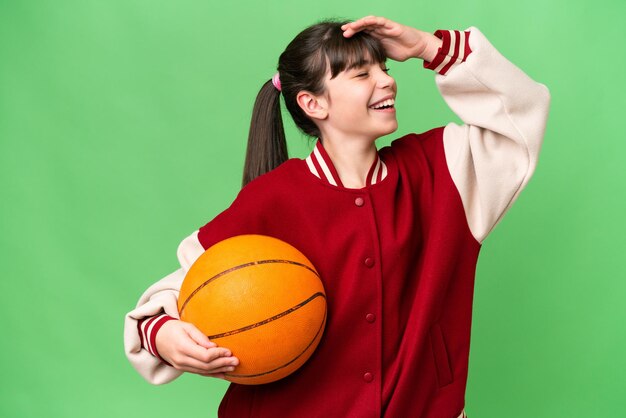 Фото Маленькая кавказская девочка играет в баскетбол на изолированном фоне, много улыбаясь