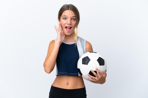 Little caucasian girl playing football isolated on white background with surprise and shocked facial expression