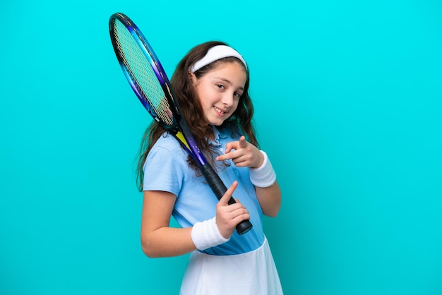 Little caucasian girl playing tennis isolated on blue background points finger at you with a confident expression