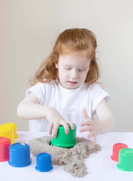 Piccola ragazza caucasica che gioca con l'istruzione precoce della sabbia cinetica a casa che prepara per il gioco dei bambini di sviluppo della scuola