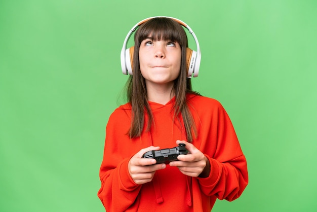 Photo little caucasian girl playing with a video game controller over isolated background and looking up