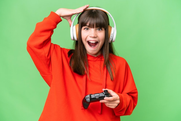 Маленькая кавказская девочка играет с контроллером видеоигры на изолированном фоне с удивленным выражением лица