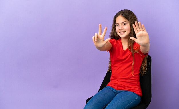 Little caucasian girl sitting on a chair isolated on purple background counting eight with fingers