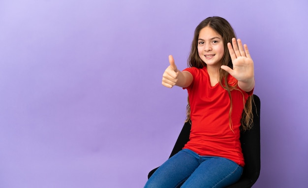 Little caucasian girl sitting on a chair isolated on purple background counting six with fingers