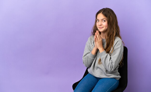 Little caucasian girl sitting on a chair isolated on purple background scheming something