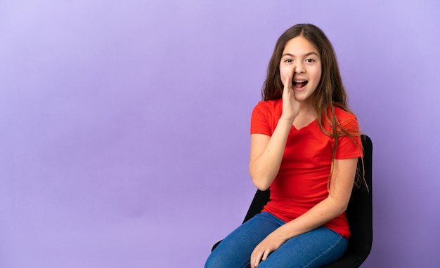 Little caucasian girl sitting on a chair isolated on purple background shouting with mouth wide open