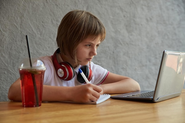 Little caucasian girl sitting at table studying with latop online education