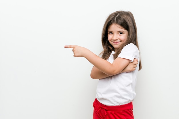 Little caucasian girl smiling cheerfully pointing with forefinger away.