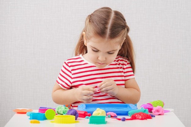 Little caucasian girl in striped Tshirt sculpts figures from plasticine play dough developing creative activities