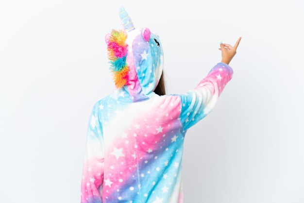 Little caucasian girl wearing unicorn pajama isolated on white background pointing back with the index finger