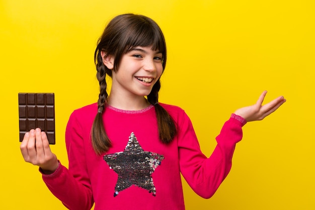 Little caucasian girl with chocolat isolated on yellow background extending hands to the side for inviting to come