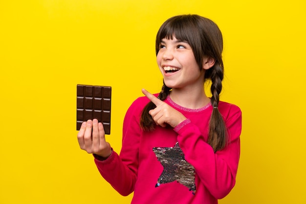 Little caucasian girl with chocolat isolated on yellow background intending to realizes the solution while lifting a finger up