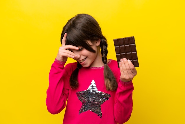 Little caucasian girl with chocolat isolated on yellow background laughing