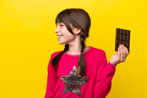 Little caucasian girl with chocolat isolated on yellow background looking side