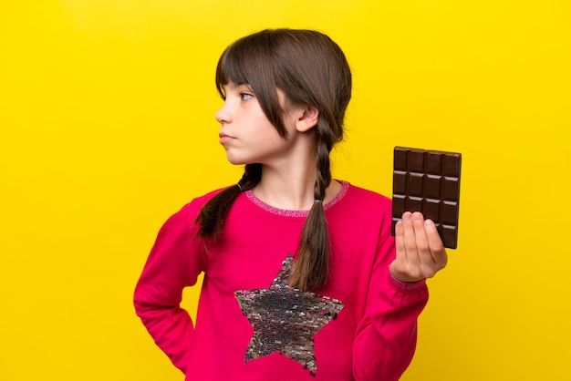 Little caucasian girl with chocolat isolated on yellow background looking to the side