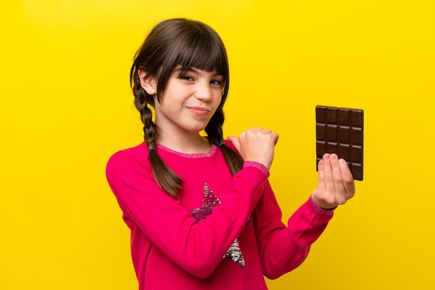 Bambina caucasica con cioccolato isolata su sfondo giallo orgogliosa e soddisfatta