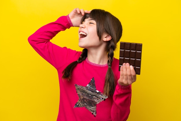 Little caucasian girl with chocolat isolated on yellow background smiling a lot