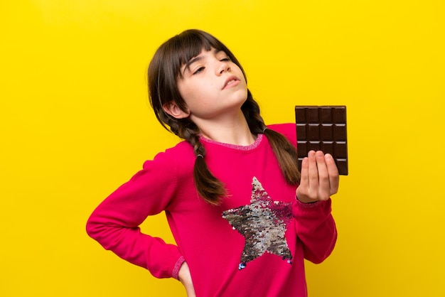 Little caucasian girl with chocolat isolated on yellow background suffering from backache for having made an effort