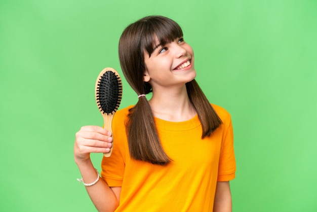 Piccola ragazza caucasica con pettine per capelli su sfondo isolato cercando mentre sorridente