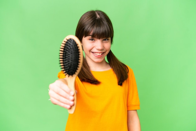 Маленькая кавказская девочка с расческой для волос на изолированном фоне со счастливым выражением лица