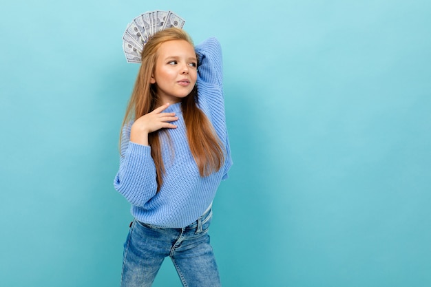 Foto la piccola ragazza caucasica con i capelli lunghi della fronte in maglia con cappuccio blu tiene molti soldi isolati su fondo blu