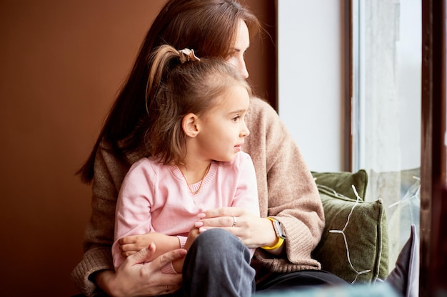 Little caucasian girl with mother looking at window and dreaming A lot of gift boxes around Happy family christmas concept