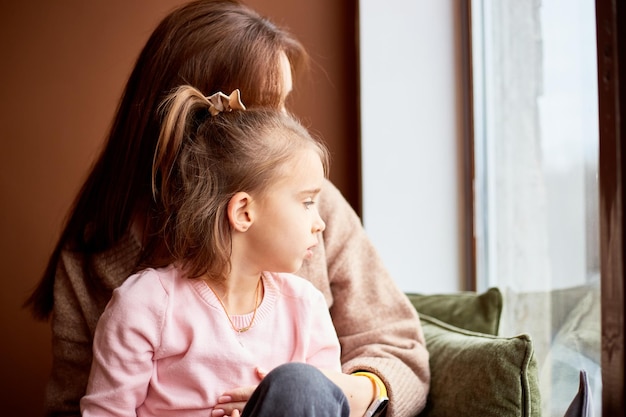 Little caucasian girl with mother looking at window and dreaming A lot of gift boxes around Happy family christmas concept