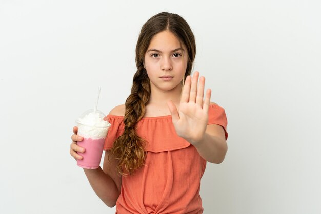 Foto piccola ragazza caucasica con frullato di fragole isolato su sfondo bianco che fa gesto di arresto