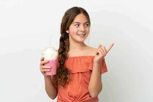 좋은 아이디어를 가리키는 흰색 배경에 고립 된 딸기 밀크 쉐이크와 어린 백인 소녀