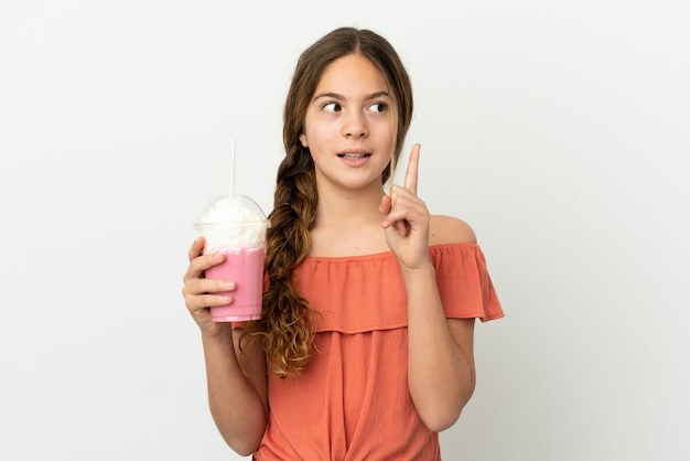 Little caucasian girl with strawberry milkshake isolated on white background thinking an idea pointing the finger up