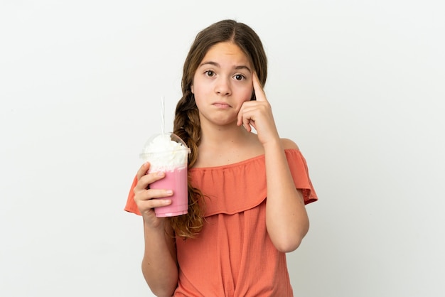 Little caucasian girl with strawberry milkshake isolated on white background thinking an idea